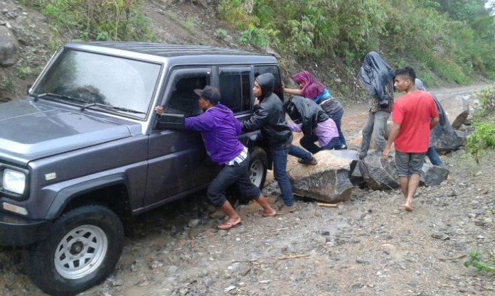 Sejumlah warga mendorong sebuah mobil yang melintasi jalan yang rusak parah menuju Elar